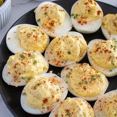 several deviled eggs are on a black plate with seasoning sprinkles