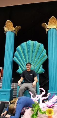 a man sitting on top of a giant blue throne next to two women laying down