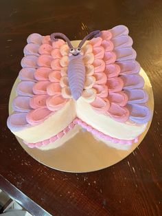 a cake decorated with pink and purple icing on a wooden table top, in the shape of a butterfly