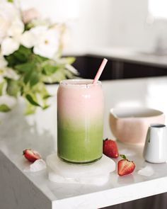 a drink sitting on top of a white counter next to some strawberries and flowers