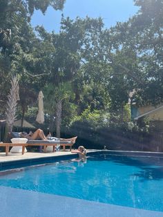 a person laying on a lounge chair next to a swimming pool with trees in the background