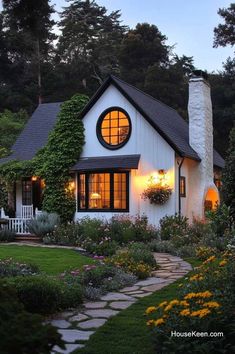 a white house with a black roof and windows in the front yard, surrounded by greenery