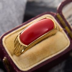 This pop of color ring features a rectangular orangey-red coral saddle. The shoulders of the ring are accented by vertical rope twists of gold. The ring is crafted in 14k yellow gold and is currently a size 7.25.  Jewelers epoxy helps secure the coral. Luxury Rectangular Ruby Ring, Heirloom Red Gold Signet Ring, Red Rectangular 14k Gold Jewelry, Rectangular Red 14k Gold Jewelry, Red Rectangular 14k Gold Ring, Rectangular Ruby Ring In Gold, Elegant Red 14k Gold Signet Ring, Art Deco Red Rectangular Jewelry, Red Rectangular Art Deco Jewelry