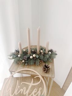 a wooden table topped with candles next to a christmas wreath and pineconi garland