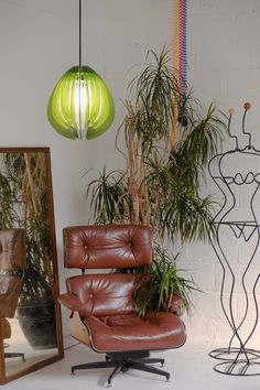 a brown leather chair sitting in front of a mirror next to a lamp and potted plant