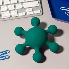 a green toy sitting on top of a desk next to a keyboard and paper clip