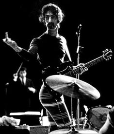 black and white photograph of a man playing the guitar in front of microphones on stage