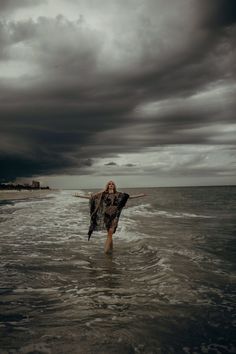 a woman walking out of the ocean with her arms outstretched in front of an overcast sky