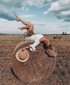 a woman laying on top of a hay bale in the middle of a field