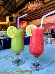 two glasses filled with different colored drinks sitting on top of a blue marble countertop