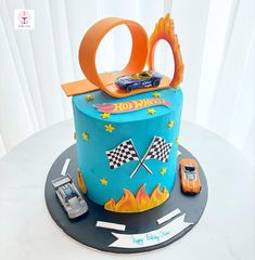 a blue cake with cars on it and an orange car in the middle, sitting on top of a table