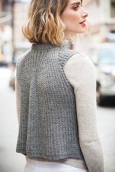 a woman standing on the street wearing a gray sweater and white skirt with her hair in a bun