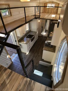 the interior of a tiny house with wood flooring and white walls, stairs leading up to an upper level kitchen area