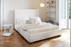 a large white bed sitting on top of a hard wood floor next to a window