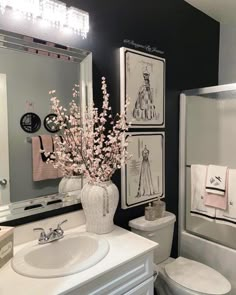 a white toilet sitting next to a sink under a bathroom mirror with pictures on the wall