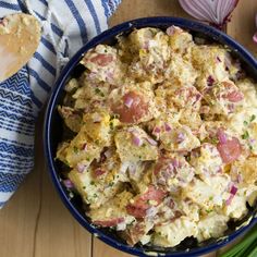 a blue bowl filled with potato salad next to green onions