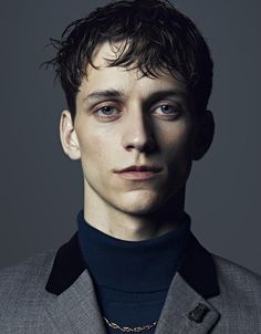 a man in a gray jacket and black turtle neck sweater is looking at the camera