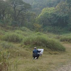 a man sitting on top of a bench in the middle of a field