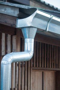 a metal gutter attached to the side of a building with wood sidings behind it