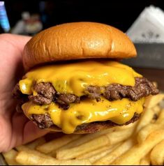 a hand holding a cheeseburger and french fries