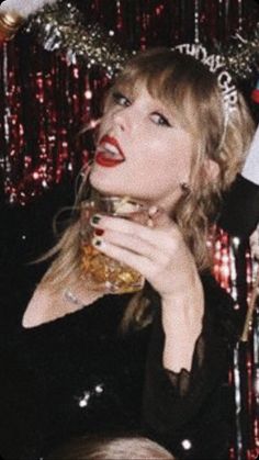 a woman with red lipstick holding a glass in front of her face and wearing a santa hat