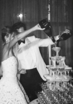 a man in a tuxedo is pouring champagne into a woman's dress