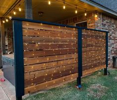 a wooden fence with string lights on it in front of a brick building and green grass