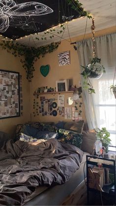 an unmade bed with lots of plants hanging from the ceiling