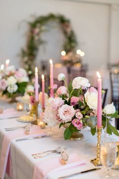 the table is set with pink and white flowers, silverware, candles and napkins