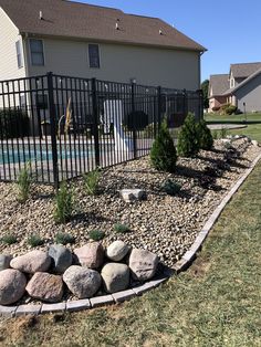 a rock garden in front of a house with a pool and fenced in yard