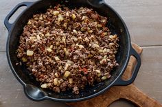 a skillet filled with meat and vegetables on top of a wooden cutting board