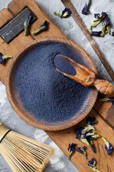 a wooden bowl filled with blue powder next to a whisk on top of a table