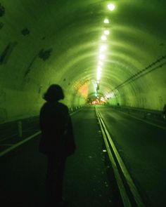 a person standing in the middle of a tunnel with lights on and dark lighting at the end