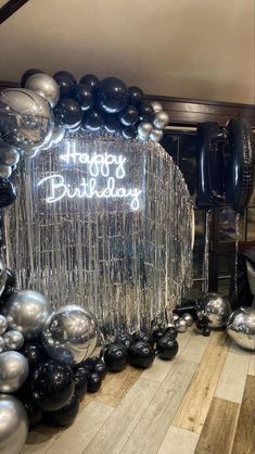 a happy birthday sign surrounded by black and silver balloons