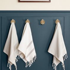 three white towels hanging on the wall next to two hooks with gold hardware and towel holders