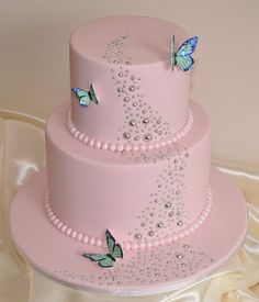 a three tiered pink cake with butterflies on the top and pearls around the edges