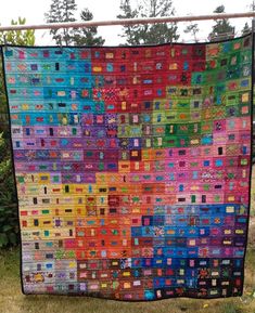 a colorful quilt is hanging on a clothesline in the grass with trees behind it