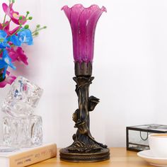 a purple glass vase sitting on top of a wooden table next to a cup and saucer