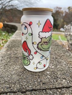 a glass with the grin on it sitting on top of a stone wall in front of some trees