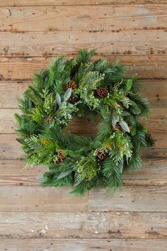 a christmas wreath hanging on a wooden wall with pine cones and evergreen leaves around it