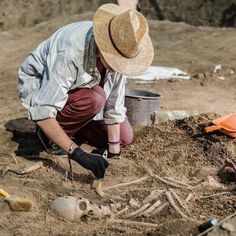 a man kneeling down in the dirt next to a pile of bones and other items