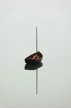 a small boat floating on top of a lake next to a tall pole with two people in it