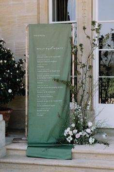 a green banner sitting on the side of a building next to white flowers and greenery