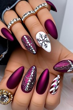 Stand out this holiday season with these stunning magenta matte almond nails! Featuring a sparkling candy cane stripe, a dazzling snowflake made of rhinestones, and silver accents, this design screams festive luxury. Perfect for Christmas parties and winter celebrations. Accessorized with gold rings for an extra touch of glam! 💅❄️🎁 #ChristmasNails #HolidayNailArt #FestiveNails #MatteNails #AlmondShapedNails #RhinestoneNails #CandyCaneNails #WinterNails #NailInspiration #GlamNails #WinterNailArt #PinkNails #GlitterNails #NailInspiration #ElegantNails #FloralNails #CozyVibes #NailDesign #AlmondNails #FestiveNails #christmasnails #novembernails #nailsaesthetic #decembernails #thanksgiving_nails #thanksgiving Multi Colored Christmas Nails, Berry Christmas Nails, Matte Christmas Nails Holidays, Sugar Plum Nails, Christmas Almond Nails Holidays, December Nails Almond, Chrome Holiday Nails, Purple Christmas Nails, Ornament Nails