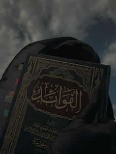 a person holding a book in their hands with arabic writing on it, against a cloudy sky