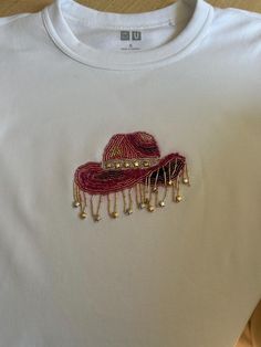 a white t - shirt with red and gold beaded hats on the chestline