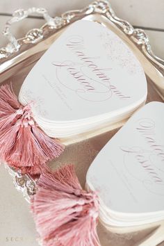 two heart shaped boxes with pink tassels on top of a silver platter