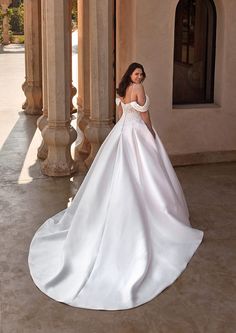 a woman in a white wedding dress is standing by some pillars and looking off into the distance