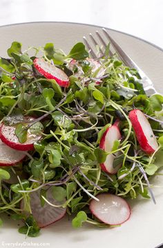 a salad with radishes and greens on a white plate next to a fork