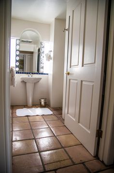 an open door leading to a bathroom with a sink, mirror and toilet paper on the floor